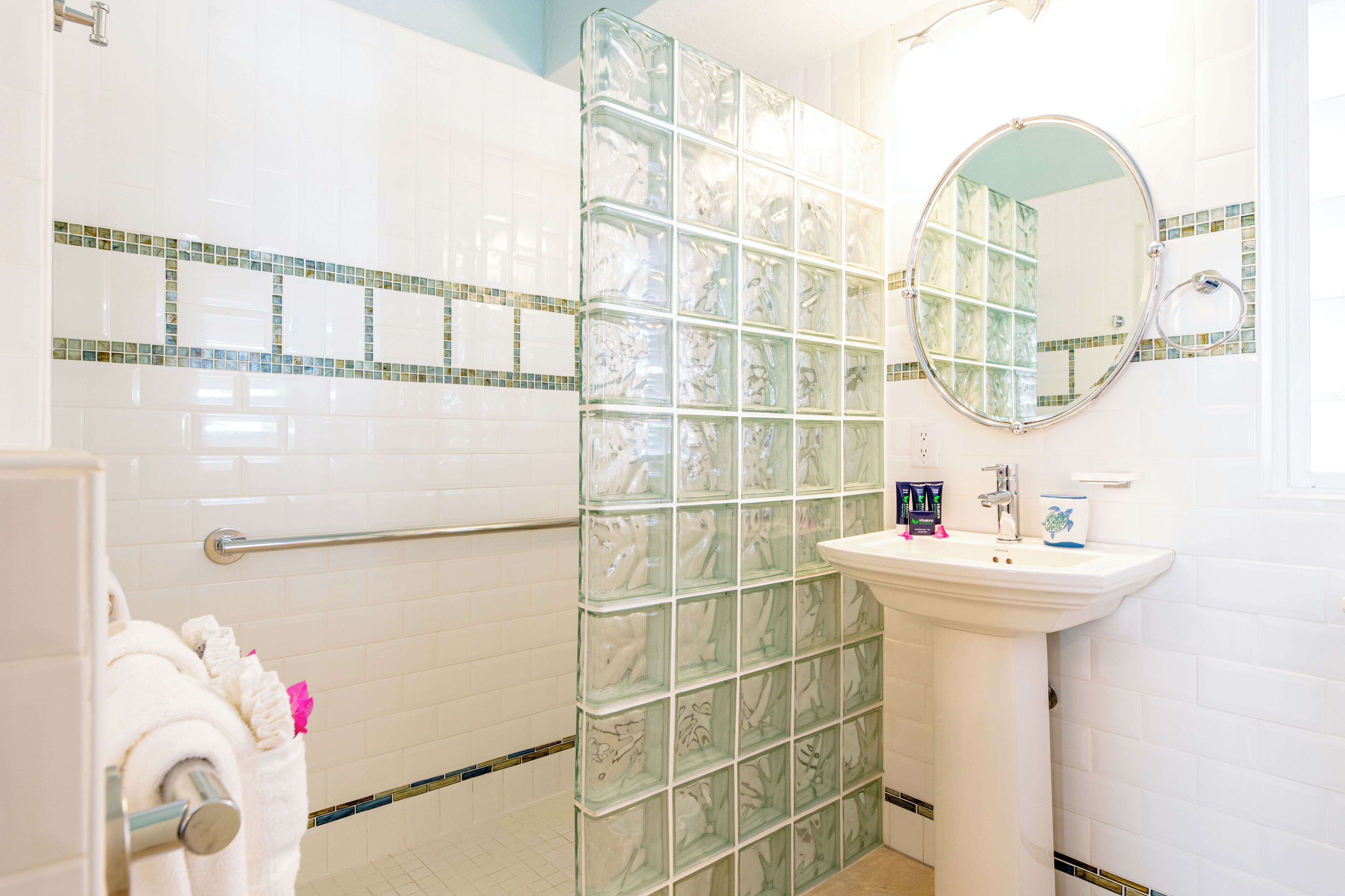 A bathroom with white tiles, a glass shower enclosure, a sink, and a mirror.