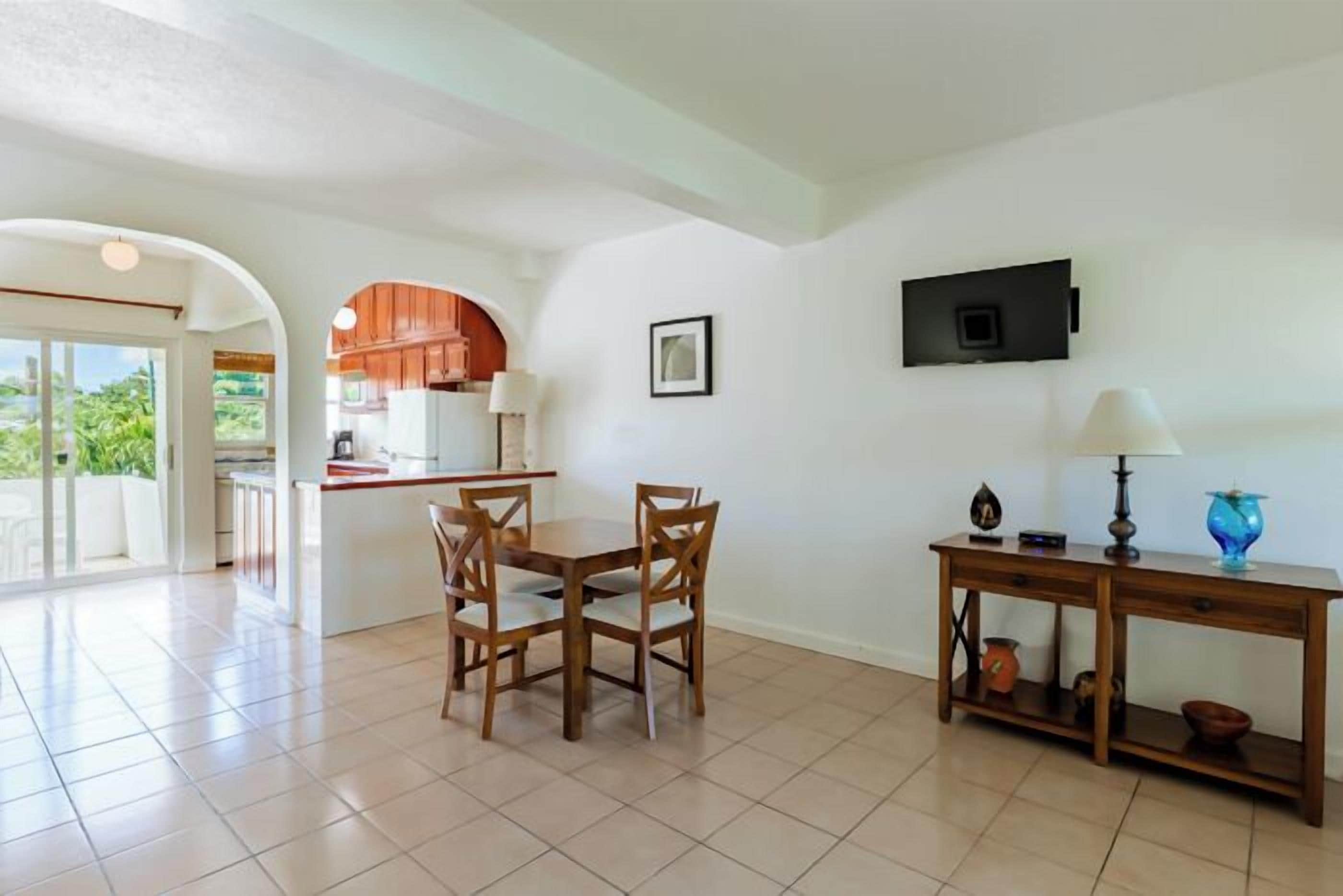 A spacious living area with a dining table, chairs, a TV, and a kitchen in the background.