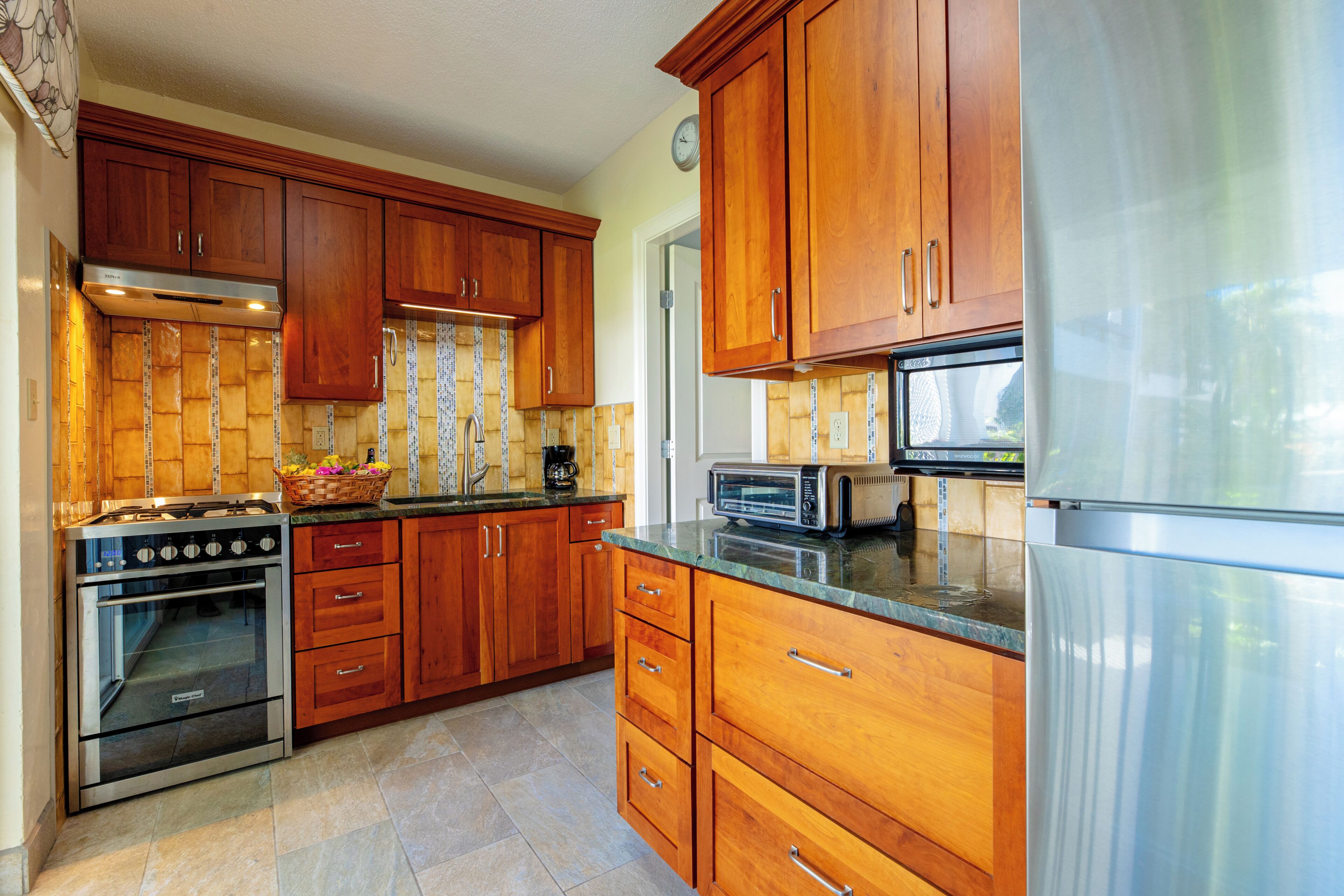 A kitchen with wooden cabinets, a stainless steel refrigerator, a toaster, and a stove.