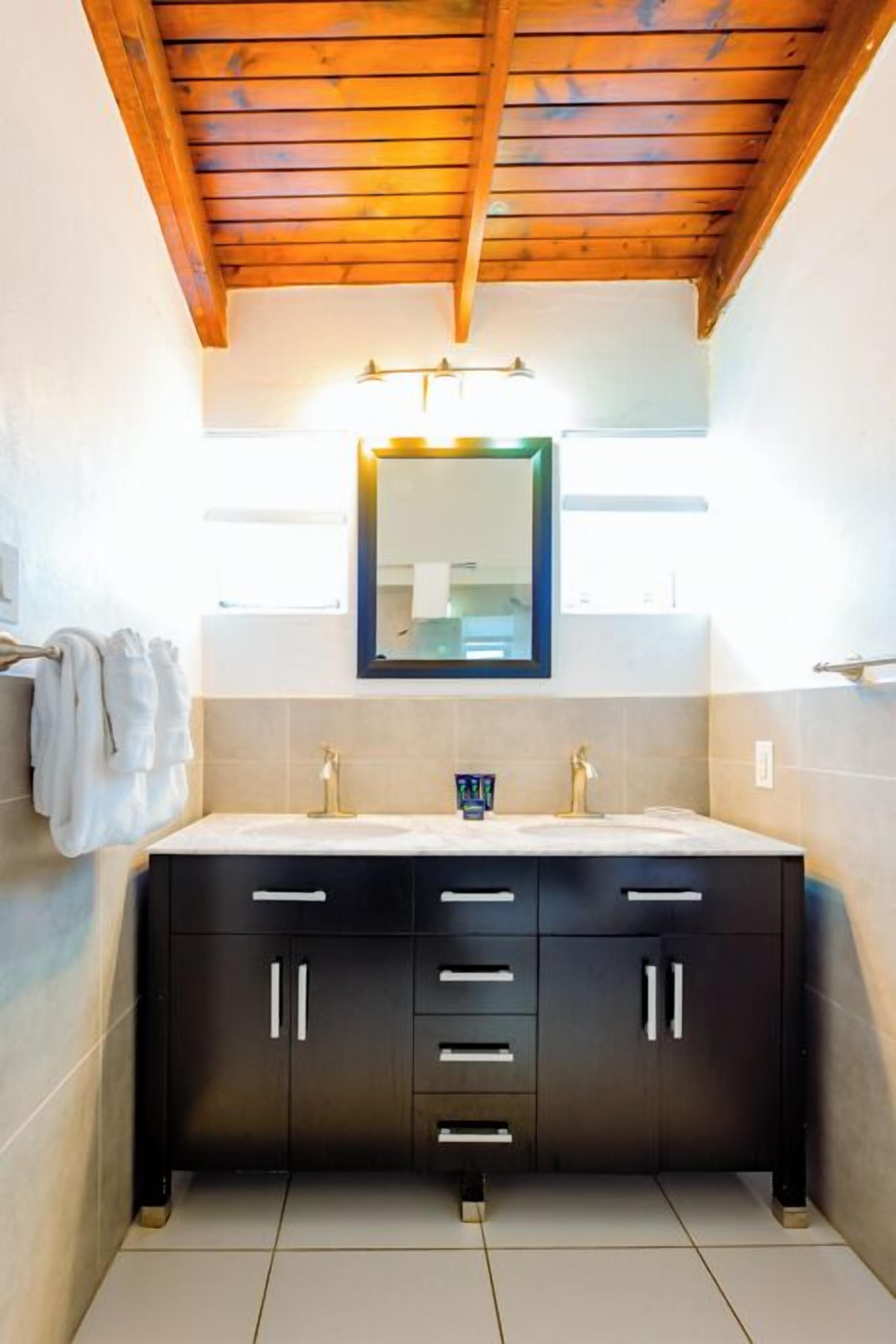A bathroom with a wooden ceiling, a large mirror, two sinks, and a tiled floor.