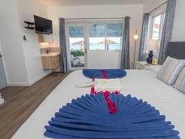 A hotel room with a bed, a TV mounted on the wall, a bathroom with a sink, and a view of the sea through the window.