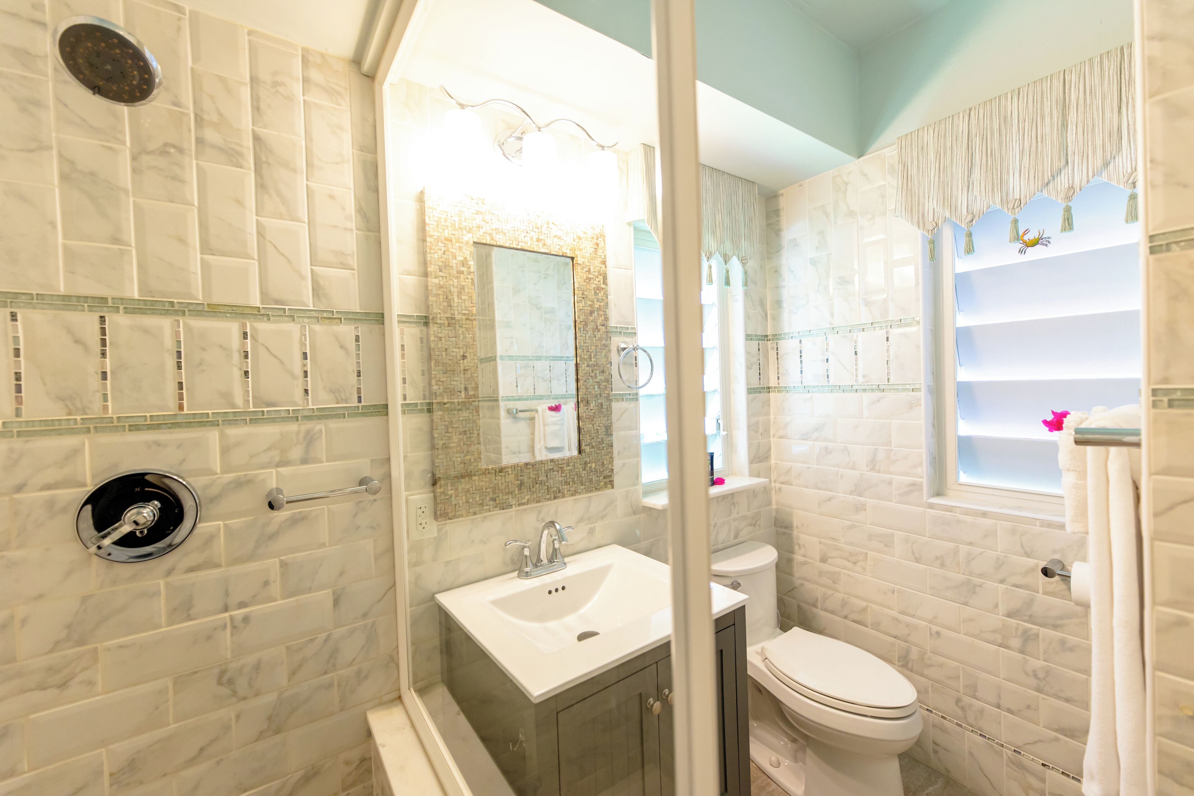 A bathroom with a glass-enclosed shower, a white sink, a toilet, and a vanity with a mirror.
