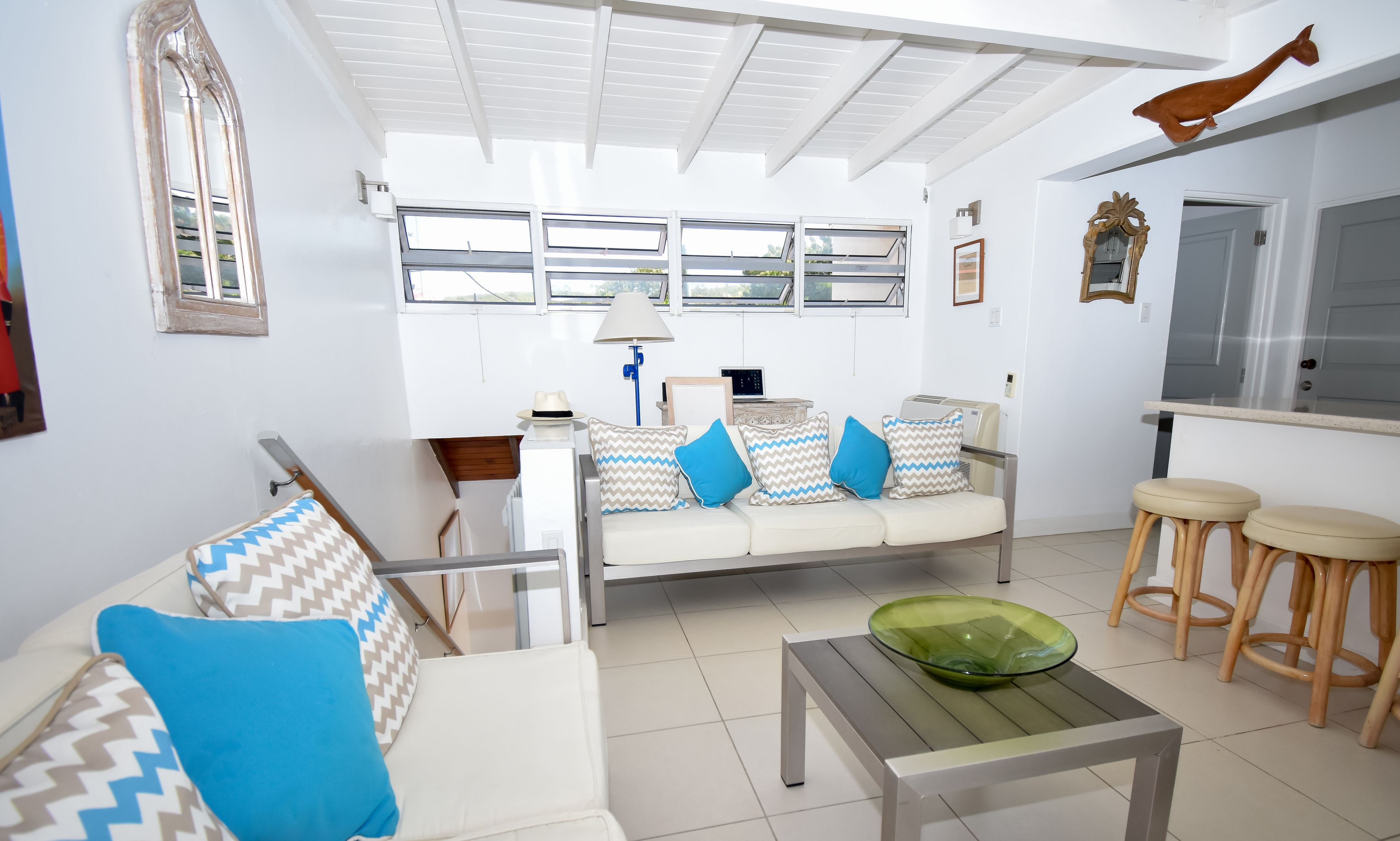 Una sala de estar con un sofá, una mesa de centro de vidrio y una zona de comedor con taburetes.