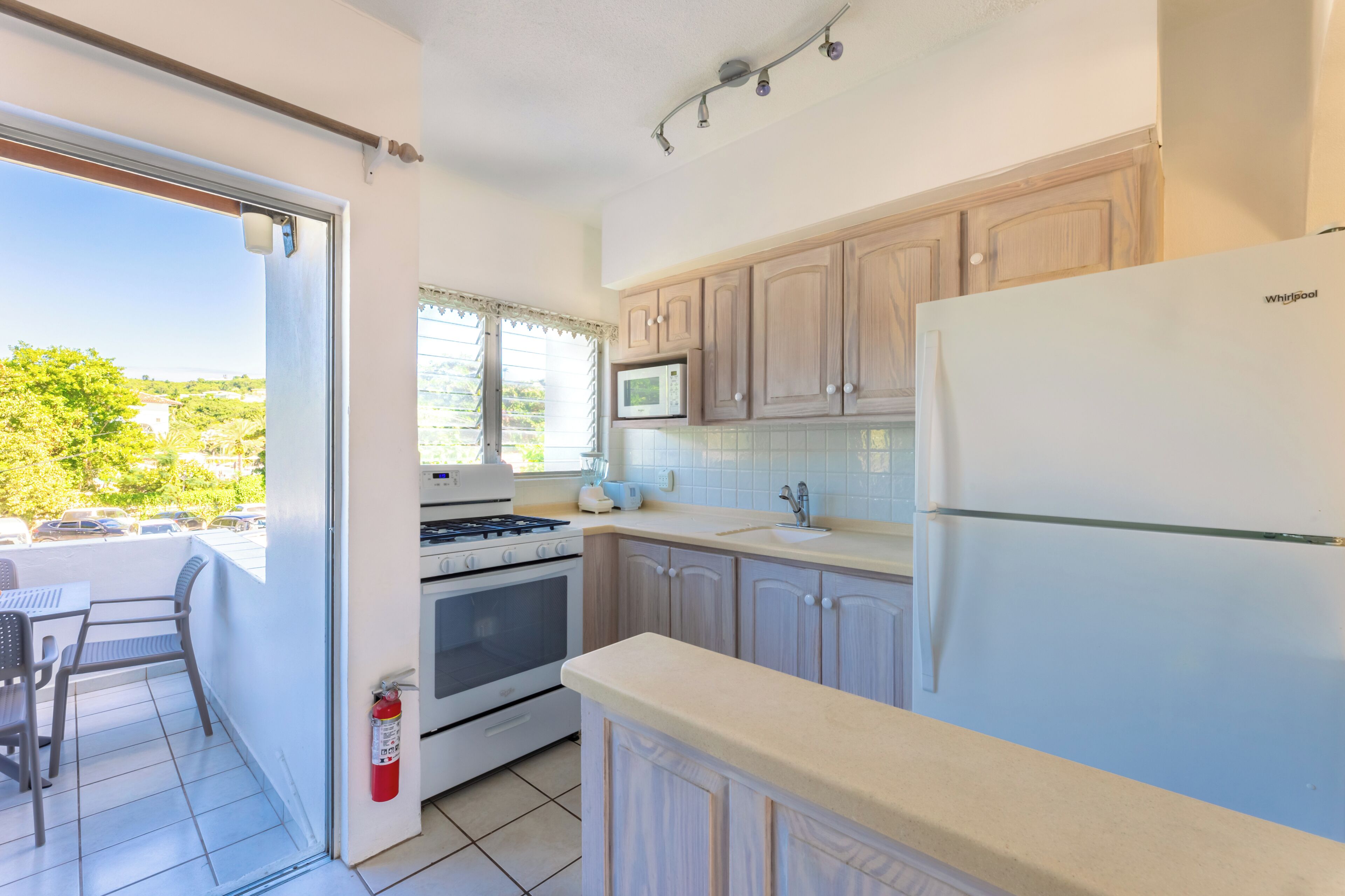 A kitchen with a stove, microwave, and refrigerator, a dining area with chairs, and a view through a sliding door.