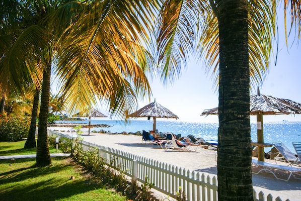 Di pantai, pasir putih, kursi berjemur, dan payung pantai