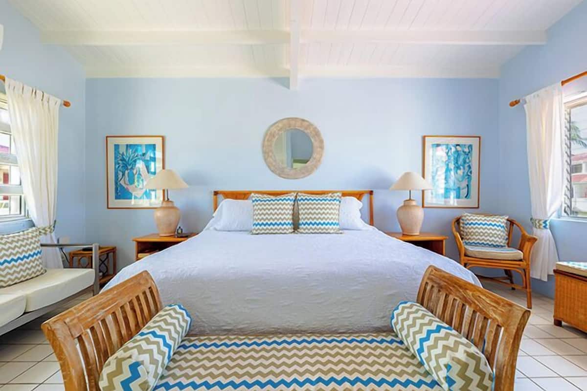 Une chambre avec un grand lit, deux tables de chevet, une chaise, une fenêtre avec des rideaux et des œuvres d’art murales.