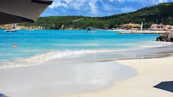 Una playa con agua turquesa cristalina, una orilla arenosa y una vista de un pueblo costero al fondo.