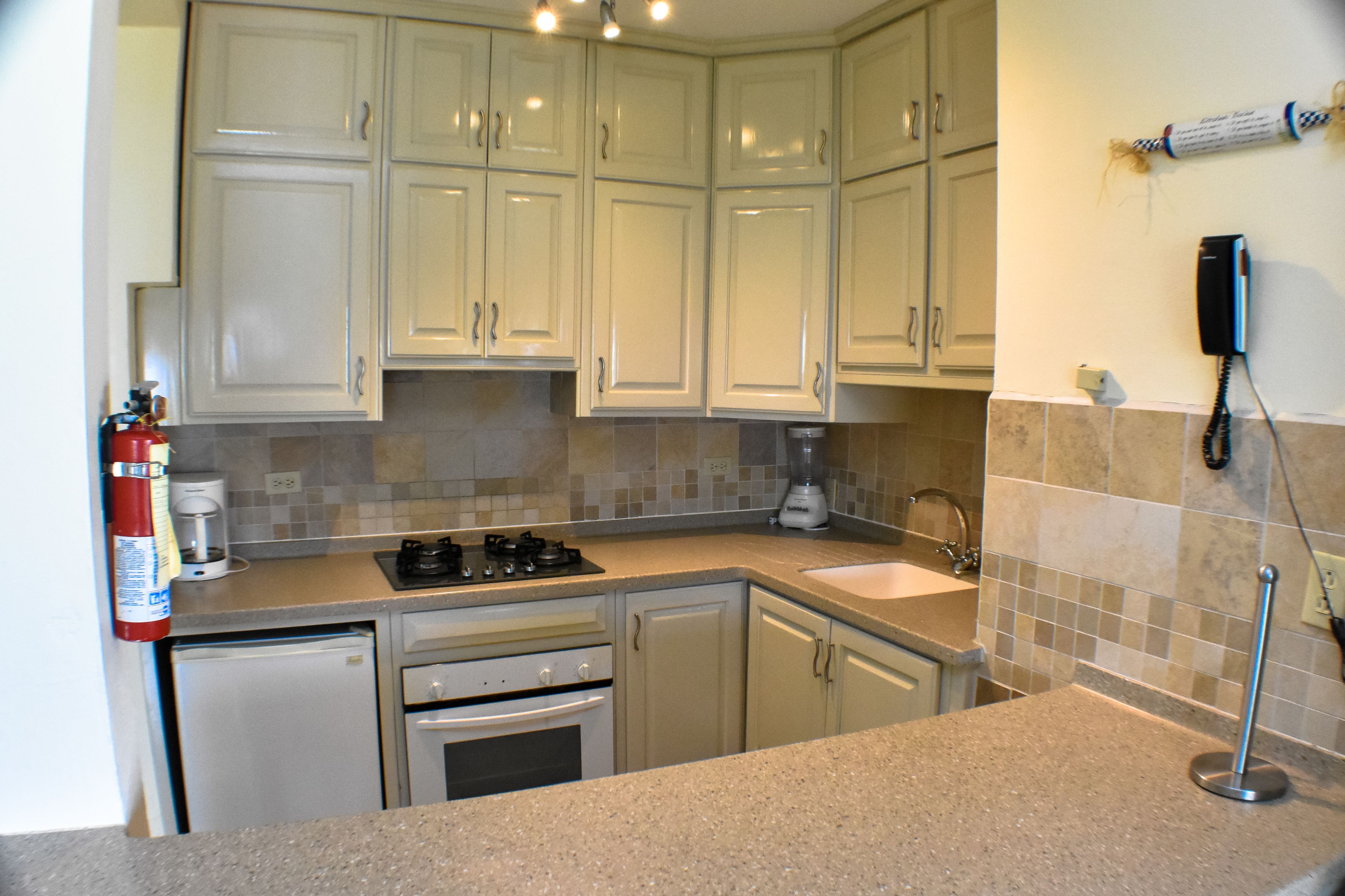 A kitchen with white cabinets, a stove, a sink, and a fire extinguisher.