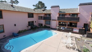 A pool area with a clear blue pool, outdoor seating, and a building with balconies. - Monarch Resort (Pacific Grove)