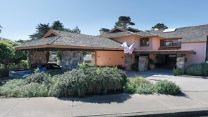 A two-story house with a stone facade, a covered patio, and a flag. - Monarch Resort (Pacific Grove)