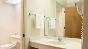 A bathroom with a toilet, sink, mirror, and hairdryer. - Monarch Resort (Pacific Grove)