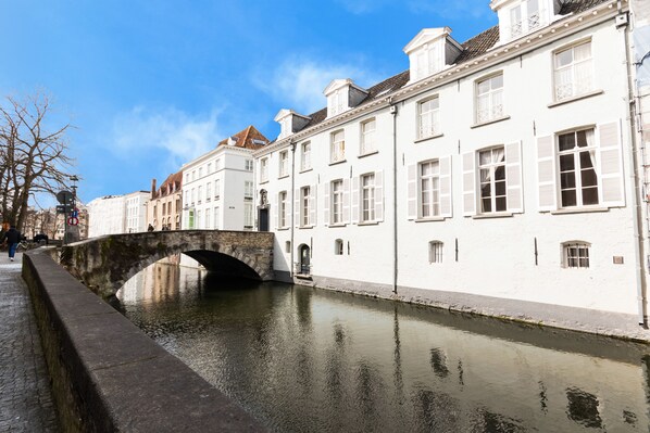A canal with a stone bridge, white buildings with shutters, and a clear blue sky.