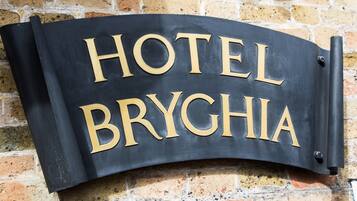 A curved sign with the words "HOTEL BRYGHIA" in gold lettering on a black background, mounted on a brick wall.