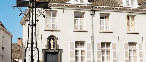 Una calle adoquinada con un farol tradicional y un edificio blanco con persianas y una estatua en la entrada.