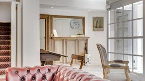 A living room with a red leather sofa, a wooden piano, and a large window with a view. - Bryghia Hotel (Bruges)