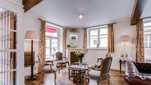 A cozy living room with wooden flooring, a fireplace, floral curtains, and a leather sofa. - Bryghia Hotel (Bruges)