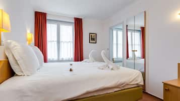 A hotel room with a bed, a bedside table, a mirror, and a window with curtains.