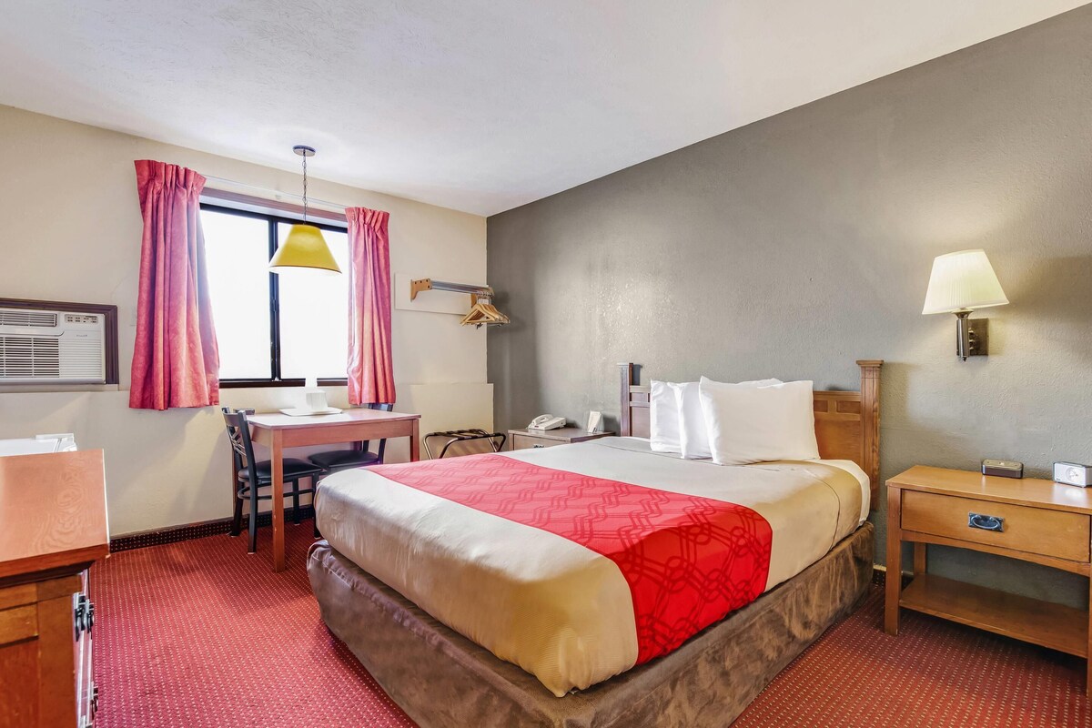 Een hotelkamer met een bed, bureau, stoel en een raam met gordijnen.