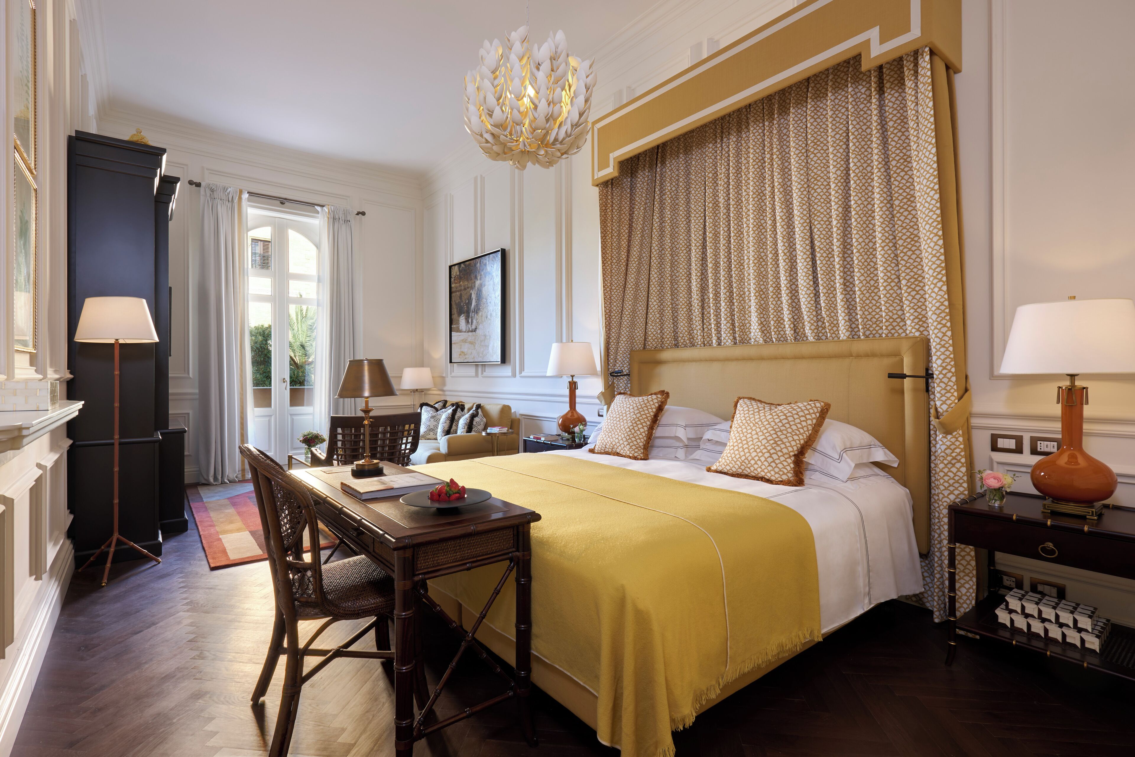 A well-appointed hotel room with a large bed, a dining area, and a chandelier.