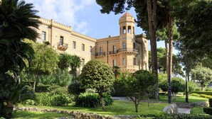 A historic building with a tower, surrounded by lush greenery and a stone pathway.