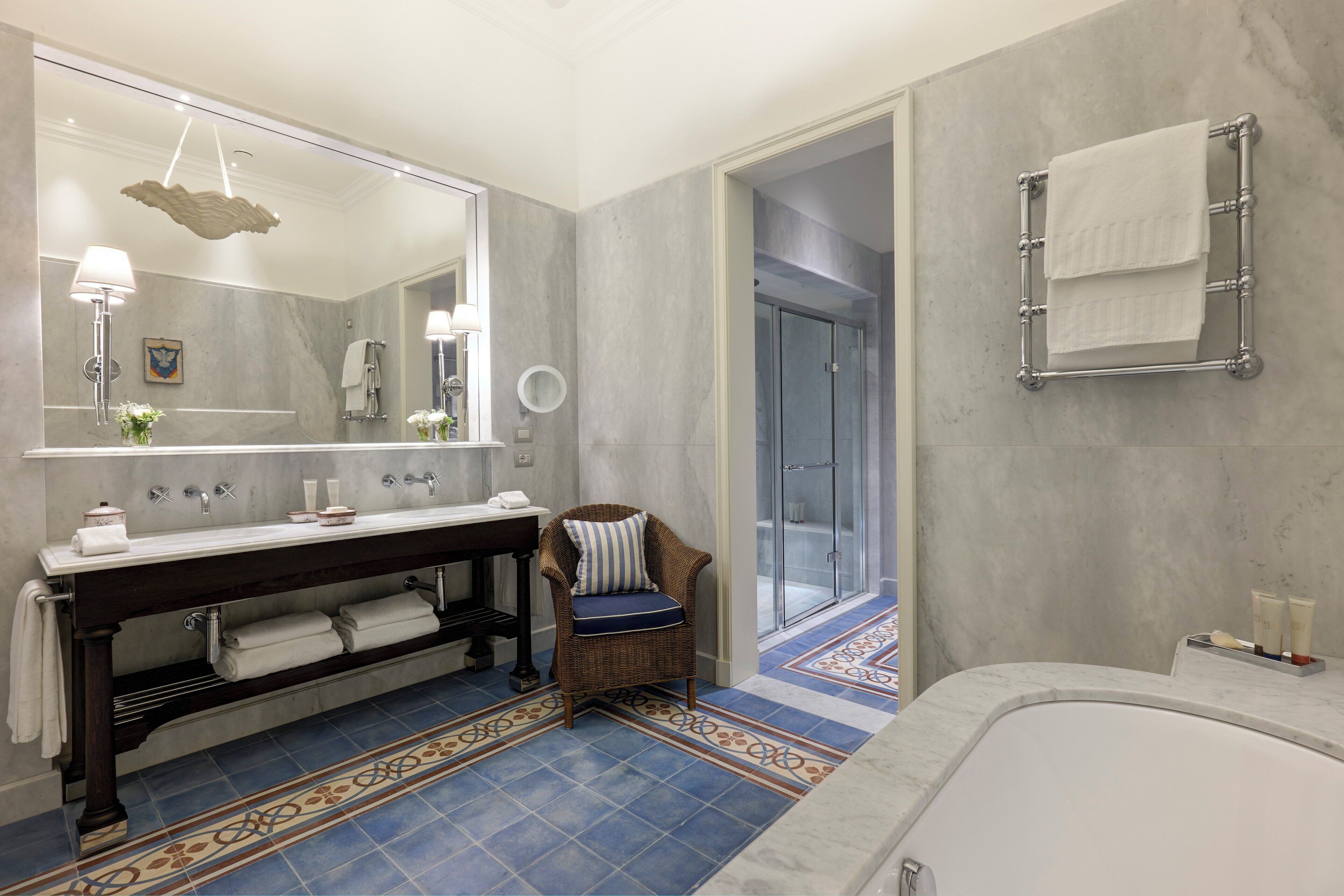 A modern bathroom with a large mirror, dual sinks, a bathtub, and a shower area.