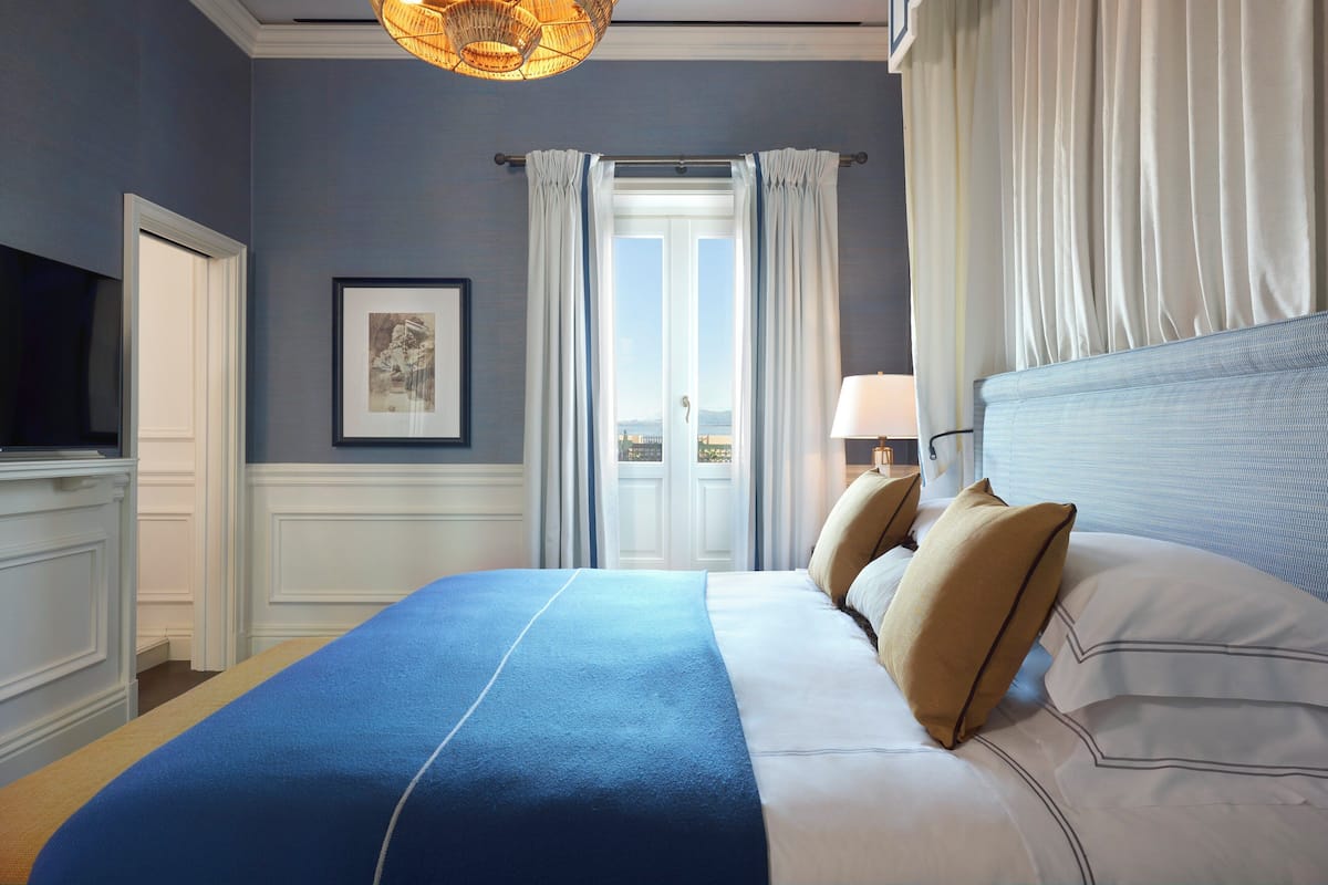 A neatly made bed with a blue and white bedspread, a television on the left, and a door leading outside.