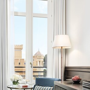A hotel room with a large window, a blue sofa, a table with a lamp, and a view of a building with a dome.
