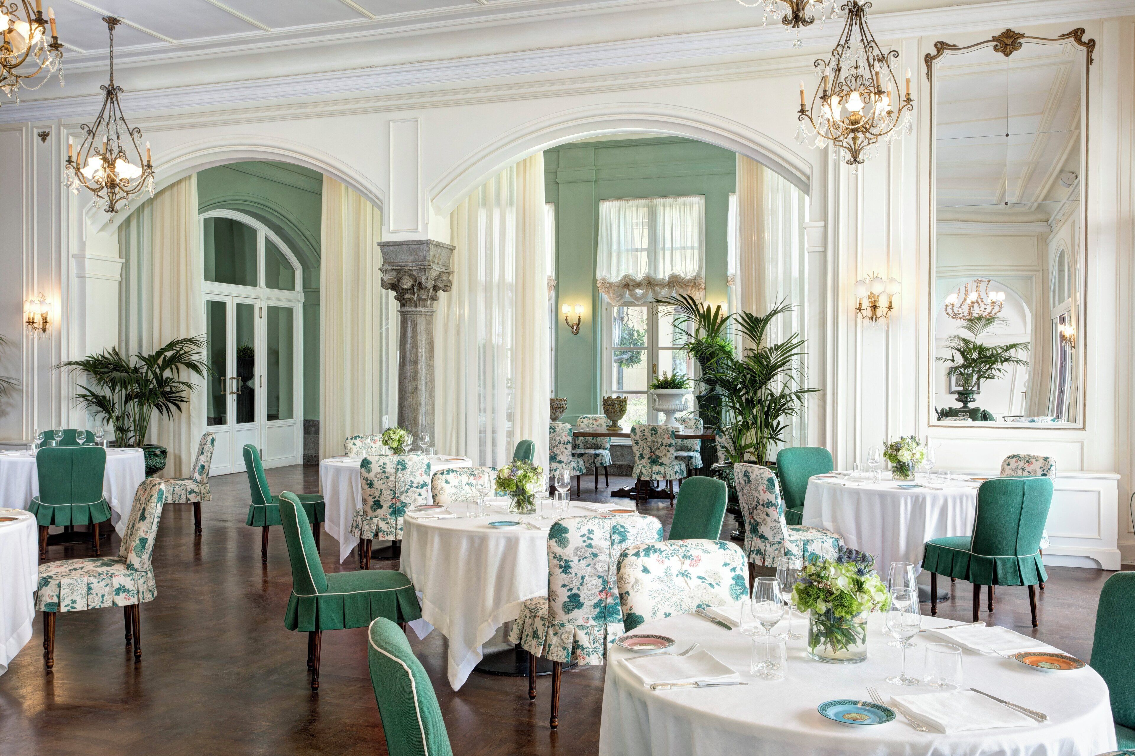Een elegant restaurant met groen bekleden stoelen, witte tafellinnen en kroonluchters.