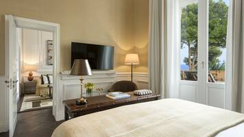 Quarto de hotel com uma cama grande, uma TV de tela plana, uma escrivaninha com abajur e vista para árvores pela janela.