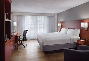 A hotel room with a large bed, a desk with a chair, a TV, and a lamp.