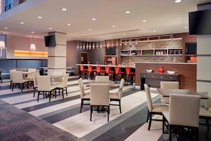 A modern hotel lobby with a bar area, seating arrangements, and a television mounted on the wall.