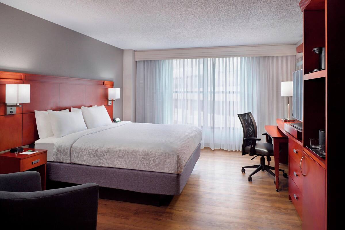 A hotel room with a large bed, a desk, a chair, and a TV.