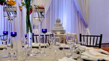 Mesa formal para cenar con copas de vino, un centro de mesa con pastel y manteles blancos.