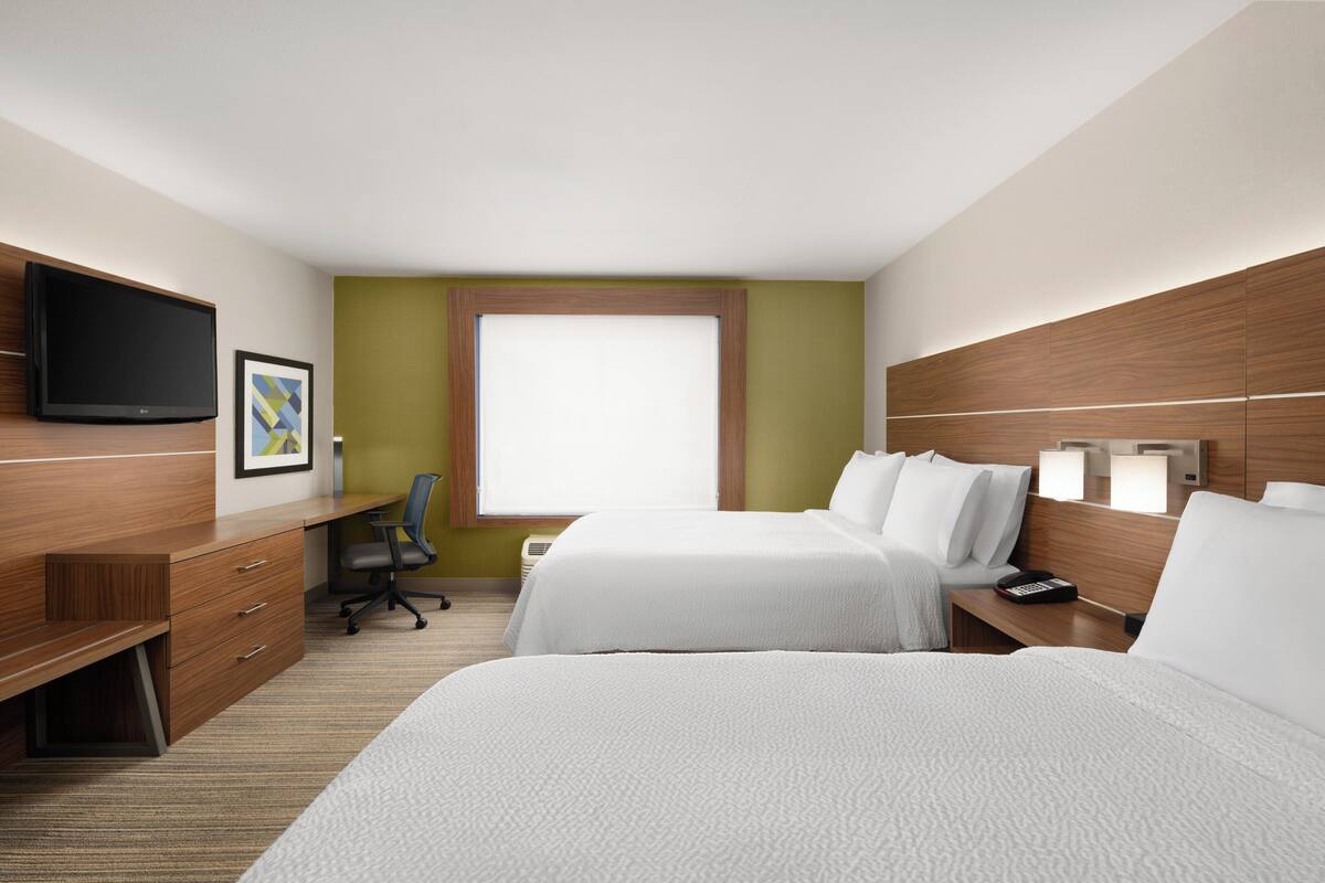 A hotel room with two beds, a desk, a chair, a TV, and a window.