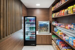 A snack and beverage vending area with a refrigerator and shelves stocked with snacks and drinks. - Holiday Inn Express San Diego - SeaWorld Area by IHG (San Diego)
