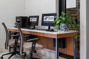 A hotel reception desk with two monitors, a coffee machine, and a potted plant. - Holiday Inn Express San Diego - SeaWorld Area by IHG (San Diego)