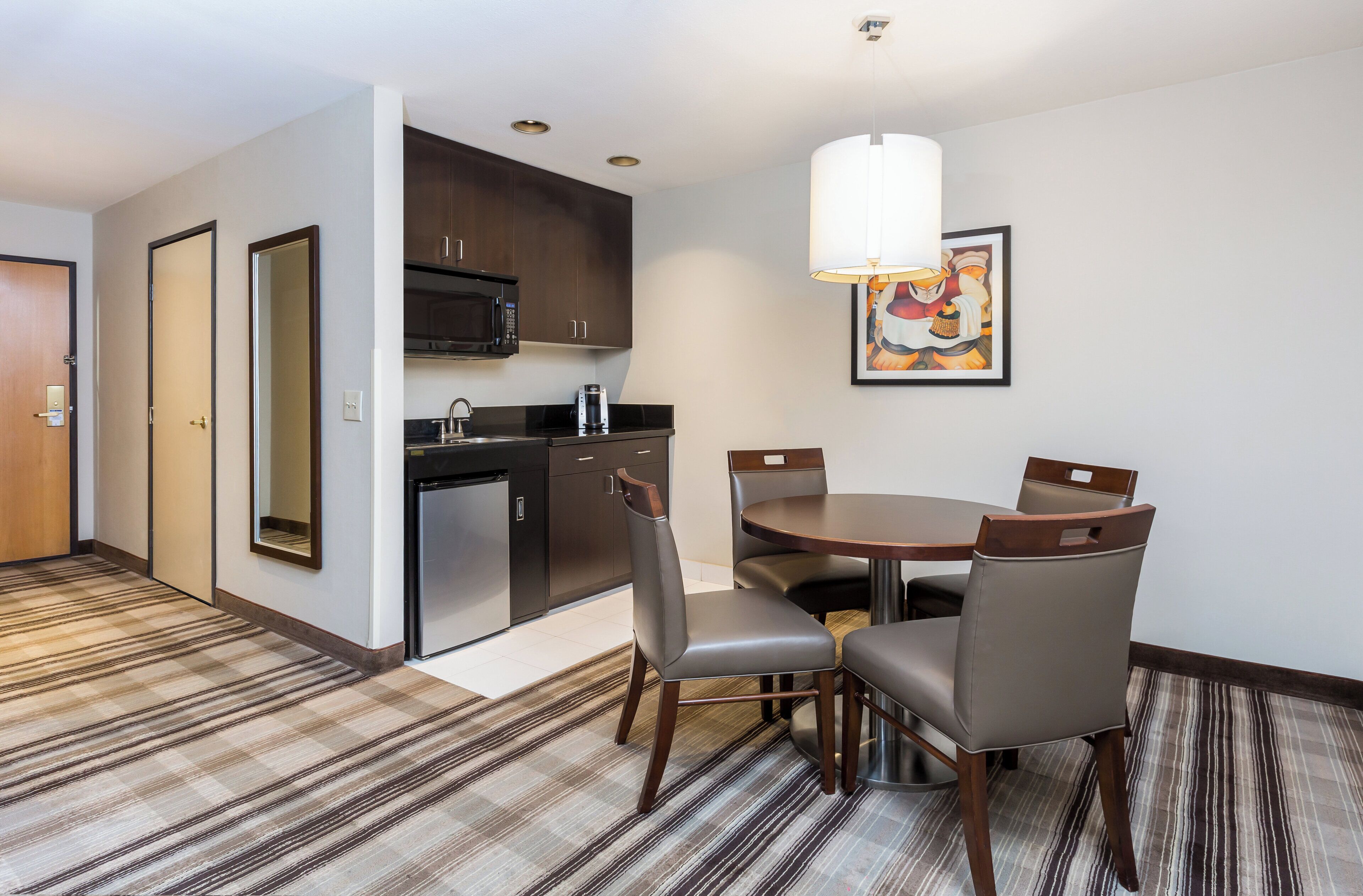 A hotel room with a dining area, kitchenette, and a large mirror.
