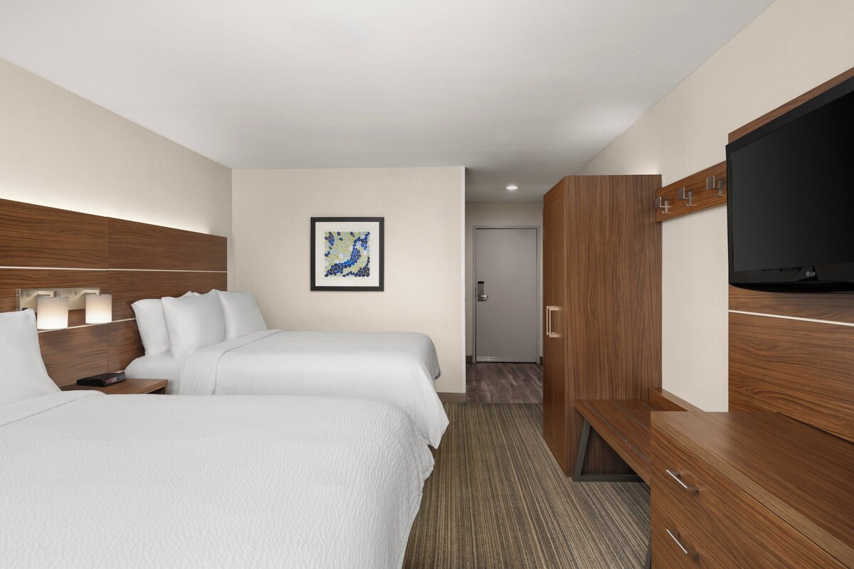 A hotel room with two beds, a flat-screen TV, a wooden wardrobe, and a framed artwork on the wall.