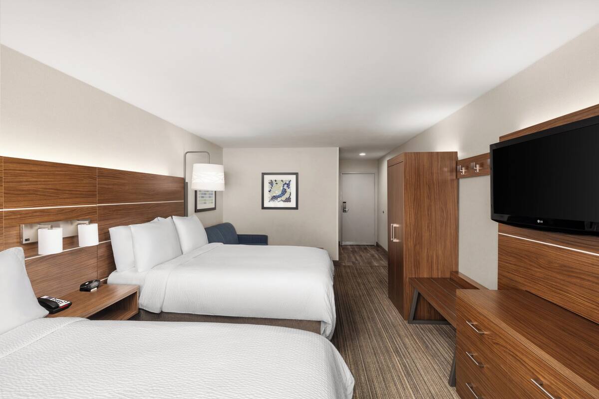 A hotel room with two beds, a television, a desk with a lamp, and a framed picture on the wall.