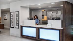 A modern reception desk with a woman standing behind it, a large digital display, and a sign for 'Haightay Inn Express'. - Holiday Inn Express San Diego - SeaWorld Area by IHG (San Diego)