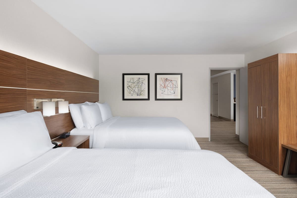 A hotel room with two beds, a wooden wardrobe, and two framed abstract artworks on the wall.