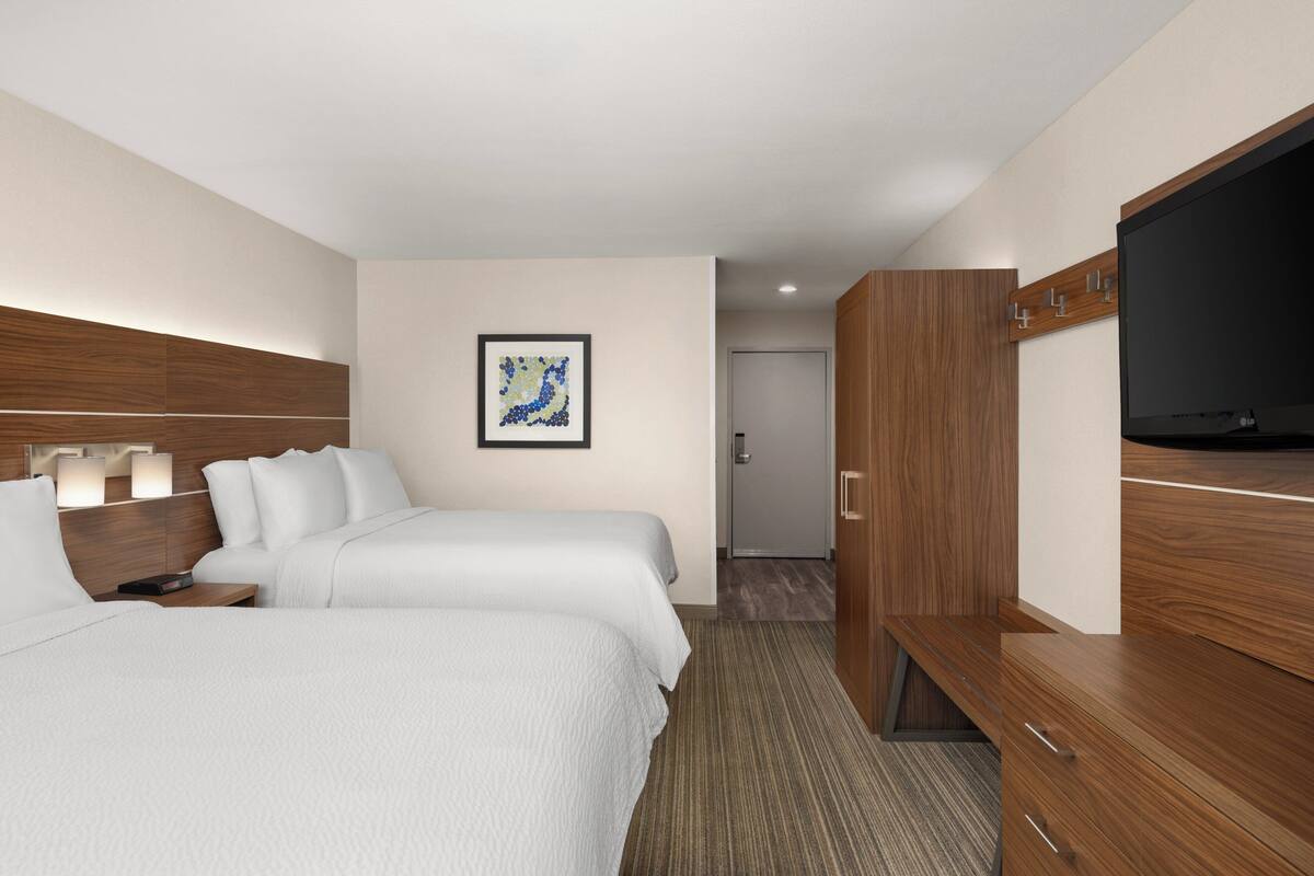 A hotel room with two beds, a flat-screen TV, a wooden wardrobe, and a framed artwork on the wall.