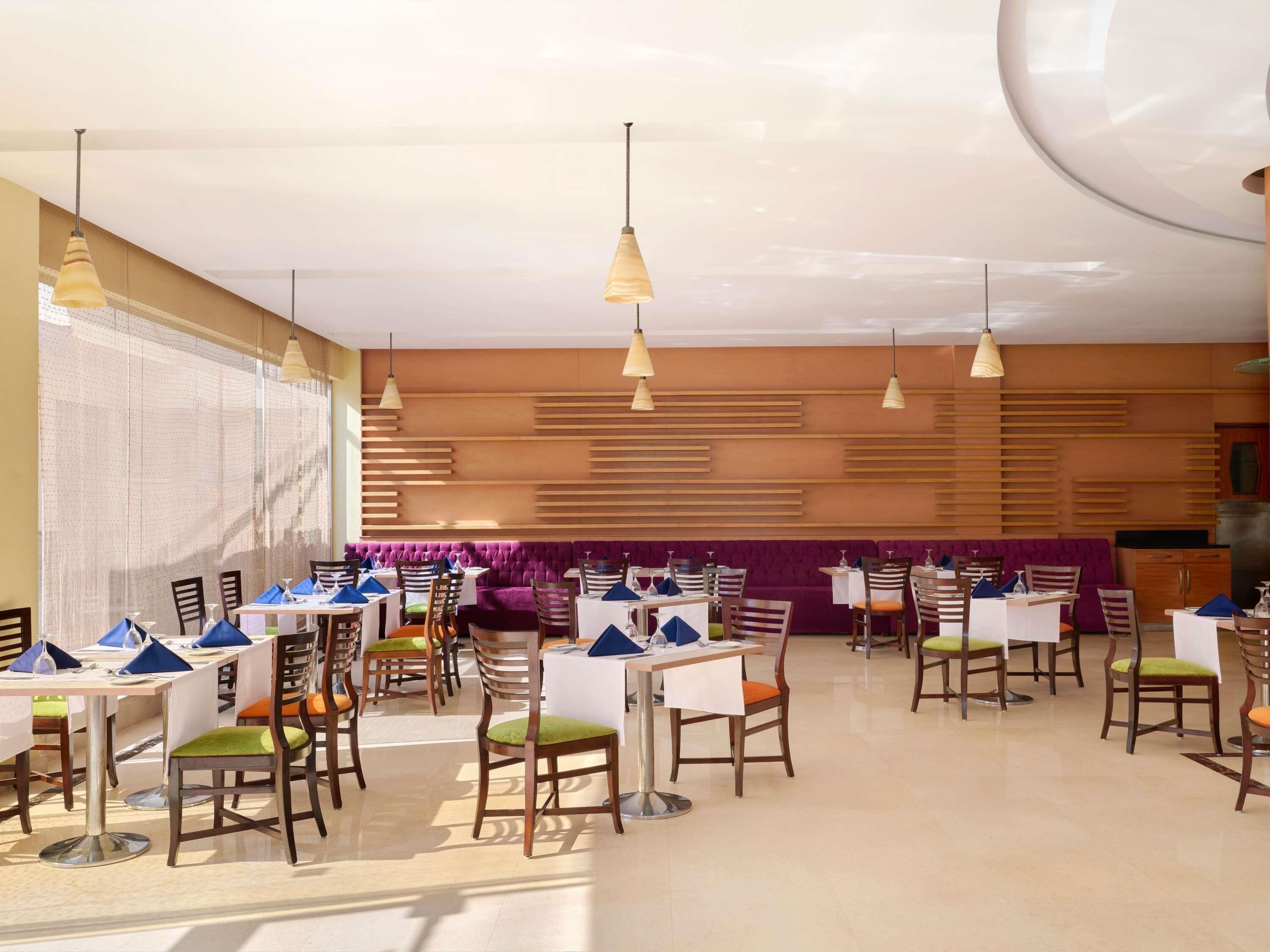 A restaurant with multiple tables and chairs, pendant lighting, and a patterned wall in the background.