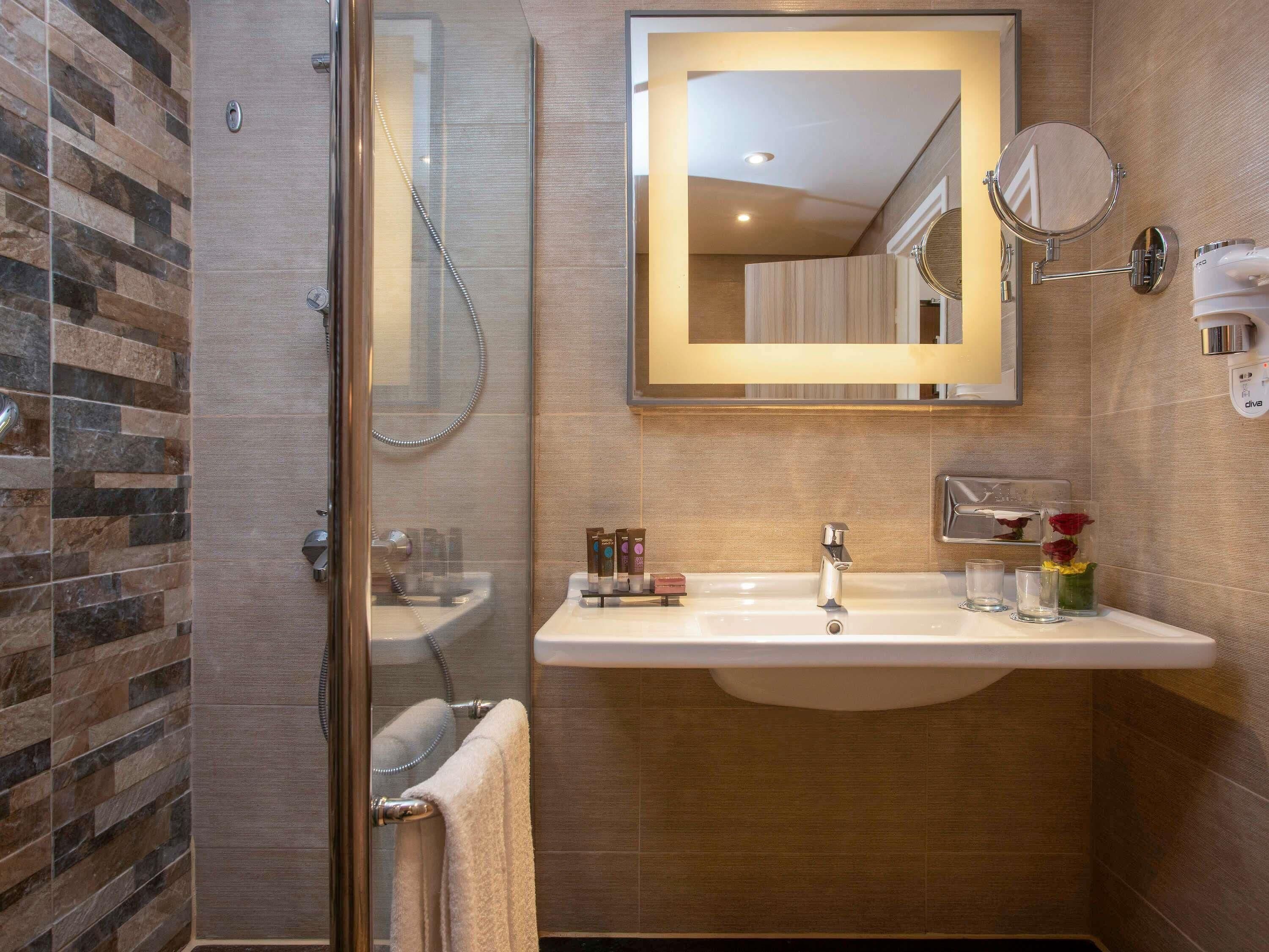 A modern bathroom with a glass shower enclosure, a sink with a mirror, and a towel rack.