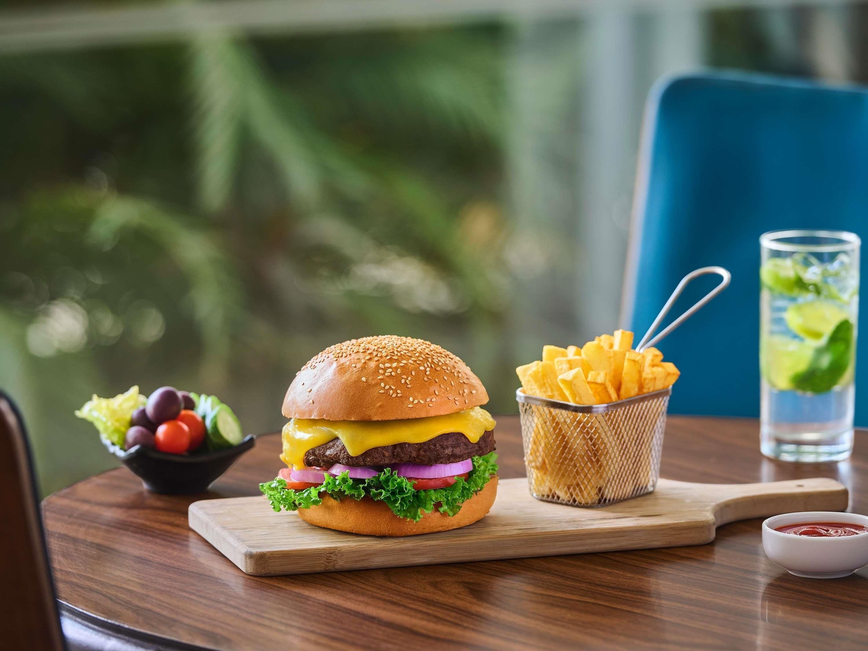 Una hamburguesa con papas fritas y una bebida sobre una mesa de madera.