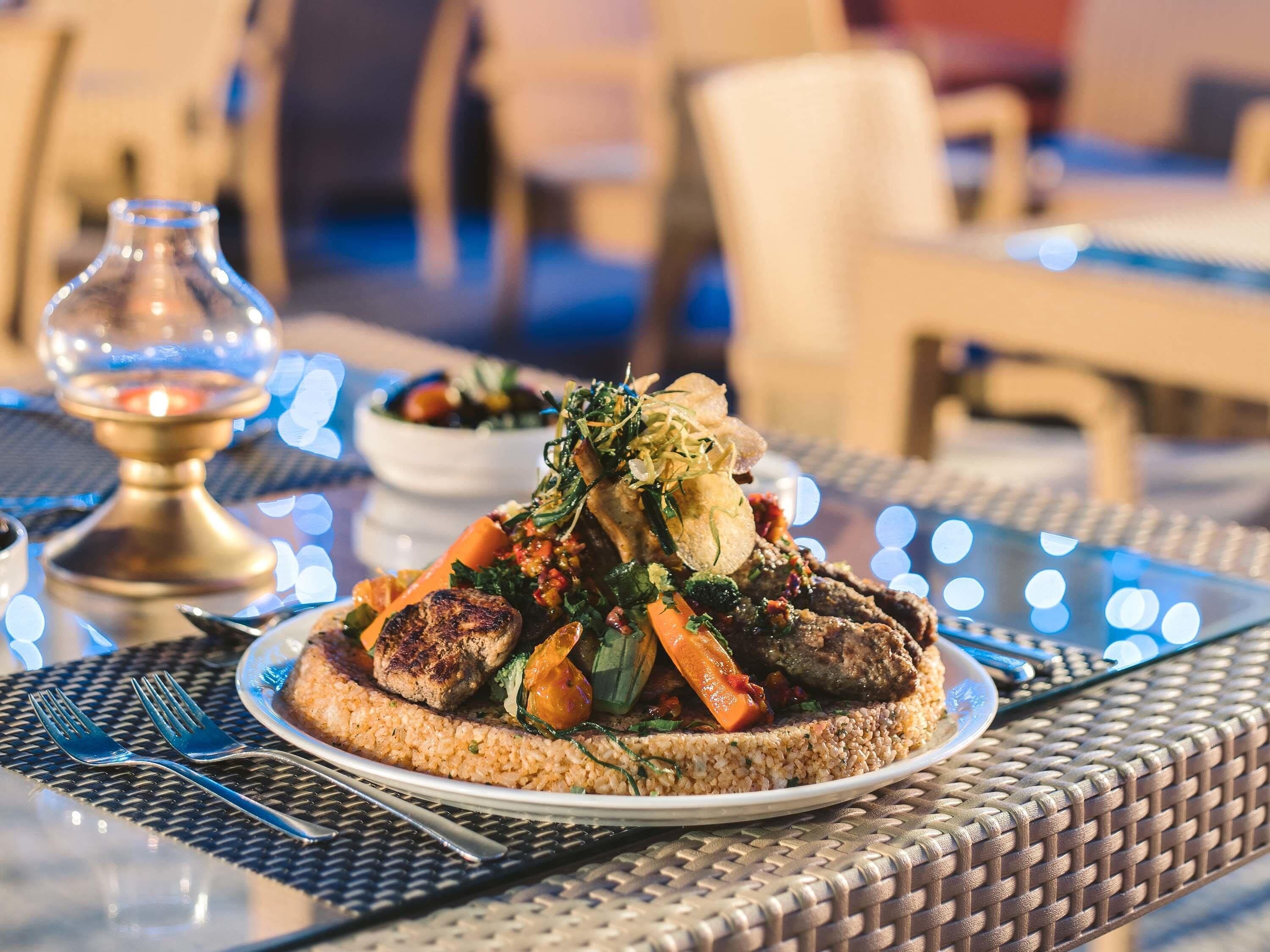 A plate of food with rice, vegetables, and meat, served on a table with a glass candle and a metal candle holder.