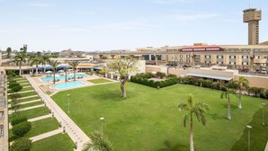 A hotel with a swimming pool, palm trees, and a view of a cityscape. - Novotel Cairo Airport (Cairo)