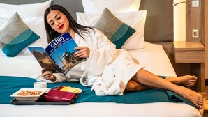 A person lying on a bed with a book titled 'CAIRO,' a tray with food, and a cup. - Novotel Cairo Airport (Cairo)