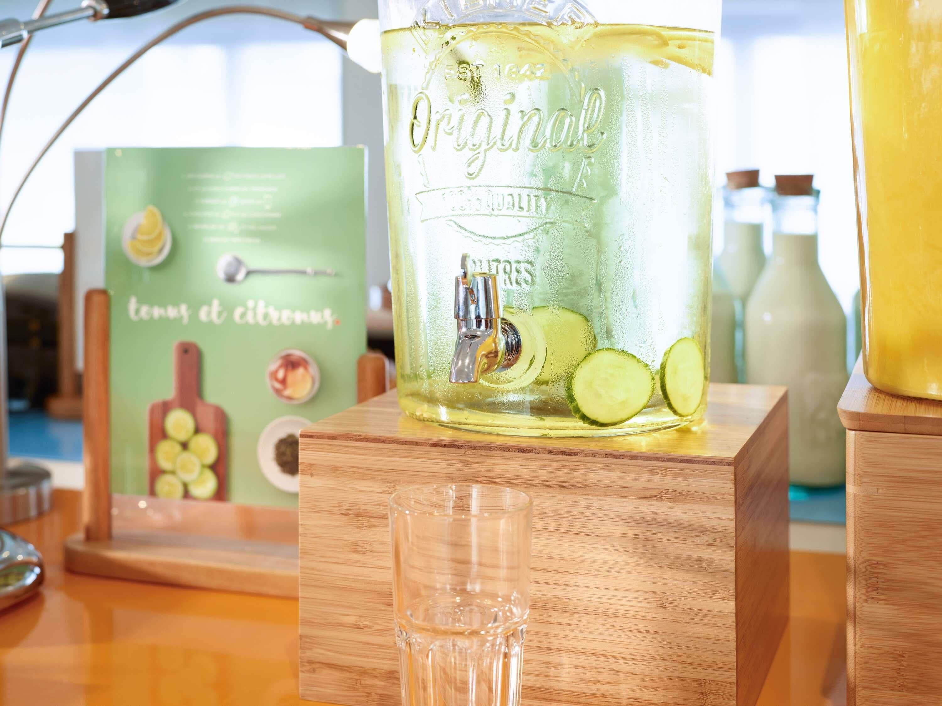 A clear glass pitcher with a label reading 'Original' and 'Cucumber' on a wooden stand.