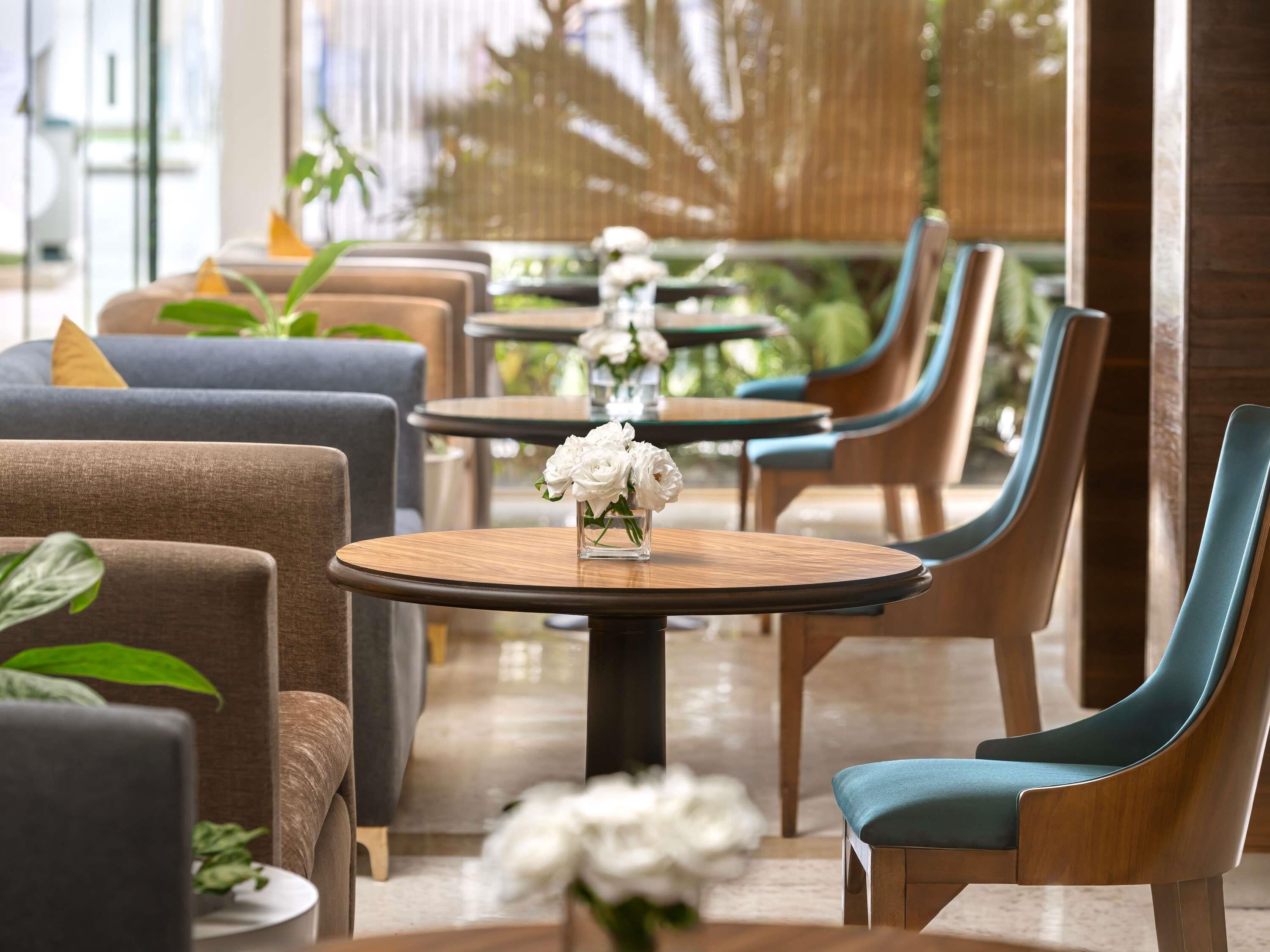 A modern indoor seating area with round tables, cushioned chairs, and potted plants.